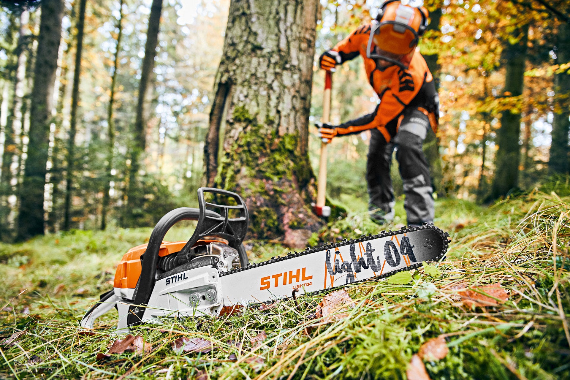 STIHL chainsaw on the ground with a person using it in the background